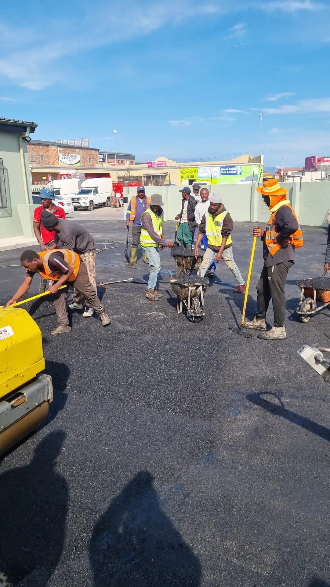 Crew raking and compacting asphalt in a commercial yard